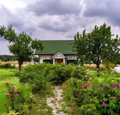 a house with a green roof and trees and flowers at Biały Domek w Ogrodzie Różanym 