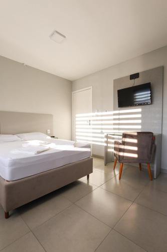 a bedroom with a large bed and a chair at Lou Suítes 11 - City Mood, estadia leve in Guarapuava