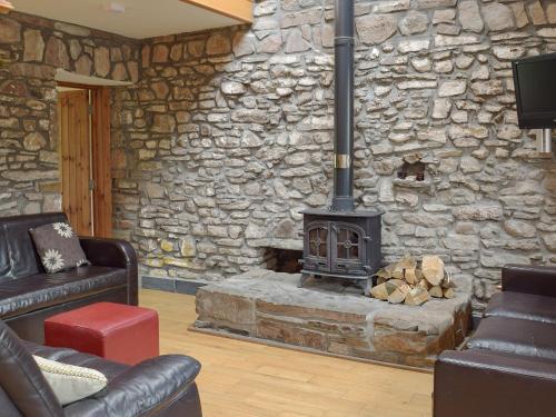 a living room with a stone wall with a stove at Pentre Cottage in Ferryside