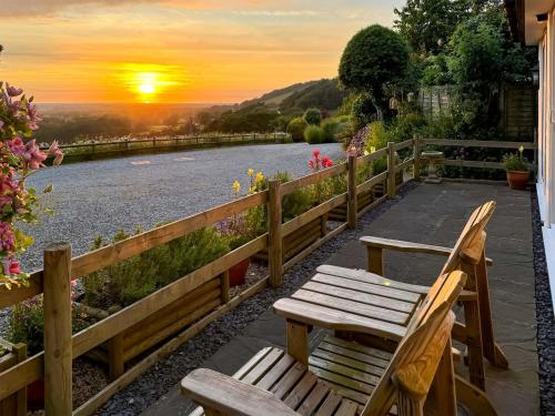 deux bancs en bois assis à côté d'une rivière au coucher du soleil dans l'établissement Beehive Cottage, à Bodfari