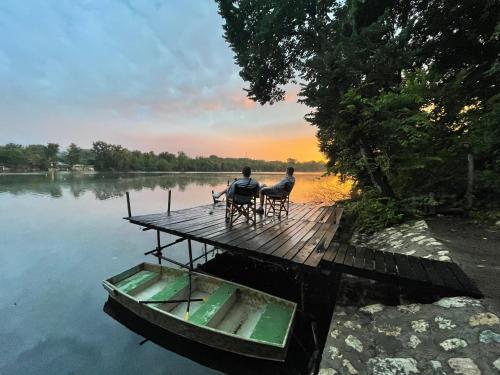 two people sitting on a dock with a boat on the water at green house at silver lake in Ostrovo