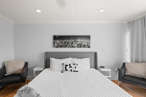 a white bedroom with a bed and two chairs at Just Beachy By Beachside Management in Siesta Key