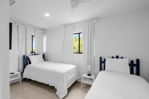 a white bedroom with two beds and two windows at Just Beachy By Beachside Management in Siesta Key