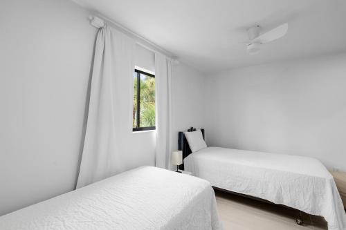 a white bedroom with two beds and a window at Just Beachy By Beachside Management in Siesta Key