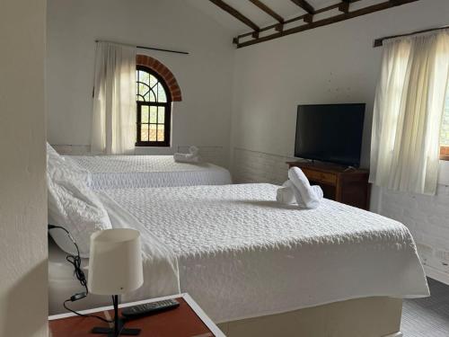 two beds in a white room with a television at Hotel Montelux in Villa de Leyva