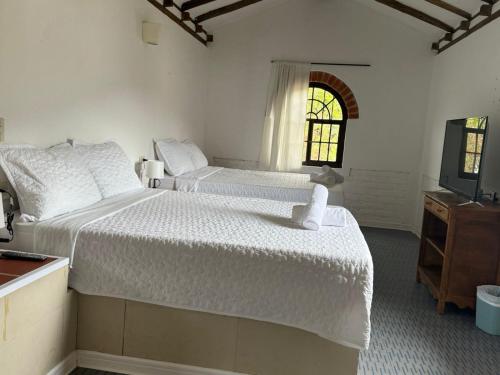 a white bedroom with two beds and a television at Hotel Montelux in Villa de Leyva