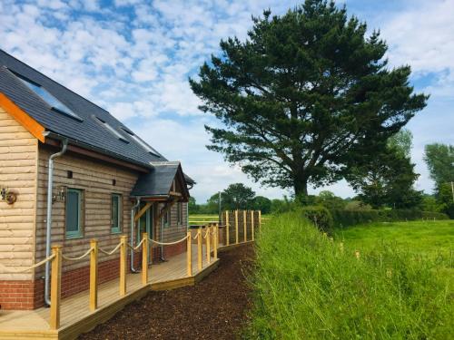 a wooden house with a fence next to a tree at Deer Den timber clad cabin with hot tub, up private lane in Cullompton