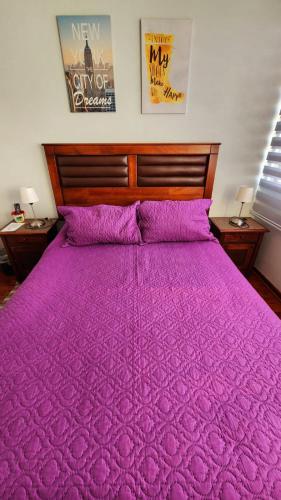 a large bed with a purple comforter and two lamps at Departamentos Amoblados Chileruca in Santiago