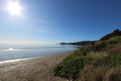 a beach with the sun shining on the water at Pohara Sands - Family Beach House in Pohara