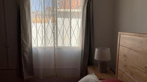 a bedroom with a window with a curtain and a lamp at Casa Chuy Barcelona in Chuy