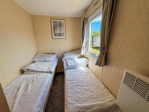 two beds in a small room with a window at Great Caravan At Valley Farm Holiday Park, Essex Ref 46583V in Great Clacton