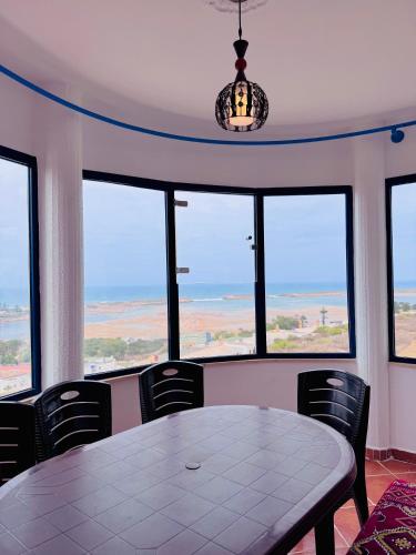 a table and chairs in a room with windows at Le grand château Vue sur Mer uniquement les familles in Oualidia