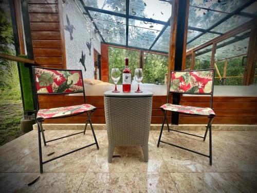 two chairs and a table with a bottle and two glasses at Hospedaje Curiquindi - Mindo Eco Lodge in Mindo
