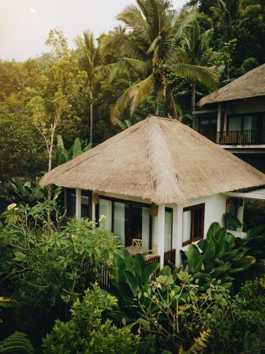 a house with a straw roof with a palm tree at Maha Hills Resort by Mahaprana Experience in Lovina
