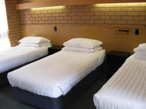 three beds in a room with white sheets and pillows at Eaglehawk Motel Bendigo in Bendigo