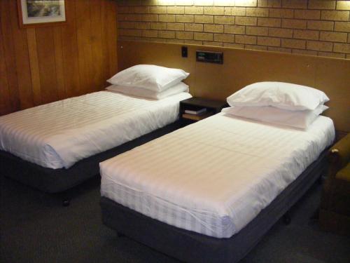 two beds in a hotel room with white sheets and pillows at Eaglehawk Motel Bendigo in Bendigo
