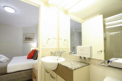 a bathroom with a sink and a bed and a mirror at Caloundra Central Apartment Hotel Official in Caloundra