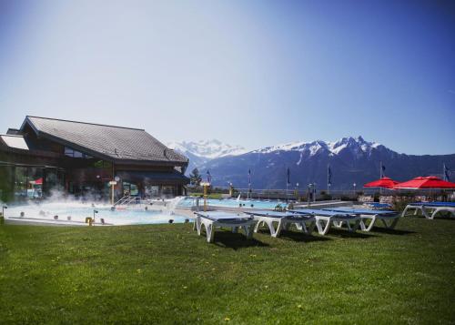 a swimming pool with tables and a building and mountains at Hôtel Les Bains d'Ovronnaz in Ovronnaz