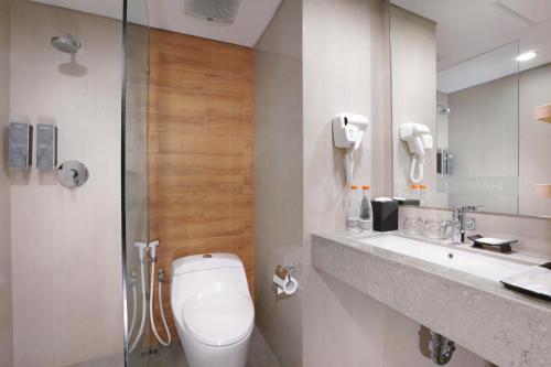 a bathroom with a toilet and a sink and a mirror at Harper MT Haryono by ASTON in Jakarta