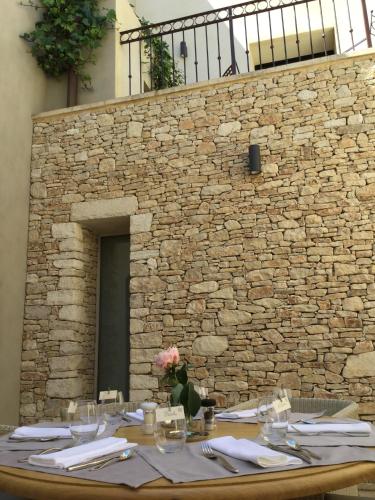 a table with plates and glasses and a stone wall at Boutique Hôtel La Villa MONTESQUIEU in Laudun