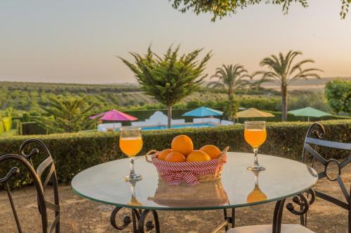 a table with two glasses of orange juice and a basket of oranges at Reservaloen Hacienda las Marciagas in Benacazón