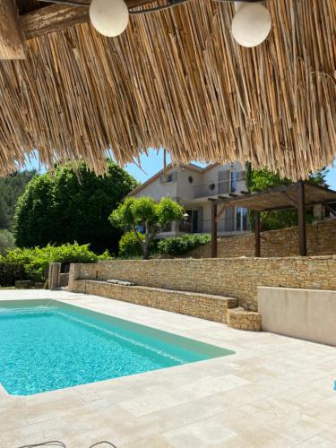 a swimming pool with a straw umbrella and a house at Le mazet Tihou - Le mas du tilleul in Le Beausset