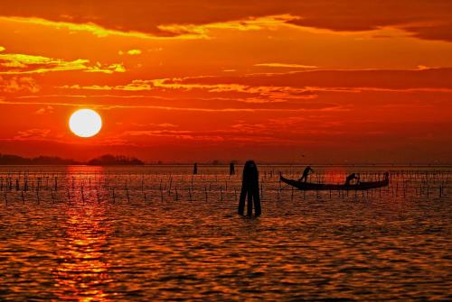 a man standing in the water with a boat at sunset at Ca' San Polo - Ferretti Hotels Collection in Venice