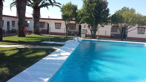 a swimming pool in front of a building with trees at Hostal las Parcelas in Conil de la Frontera