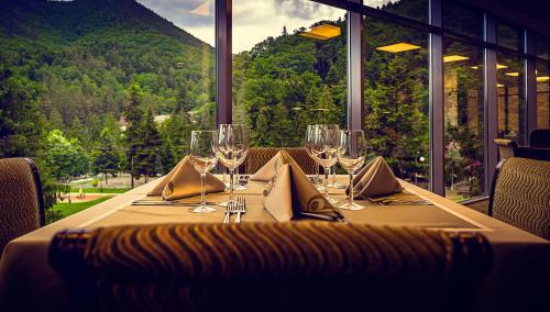 a table with wine glasses and a view of a mountain at Hotel Perla in Slănic-Moldova