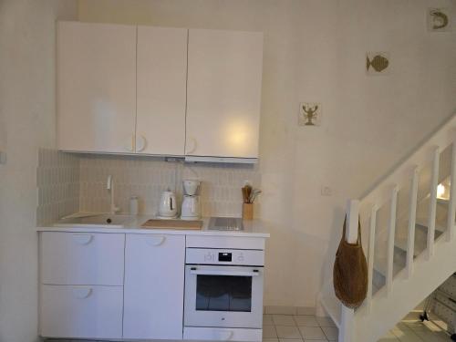 une cuisine avec des armoires blanches, un évier et une cuisinière dans l'établissement Maison entièrement restaurée et meublée à neuf, à Saint Cyprien Plage