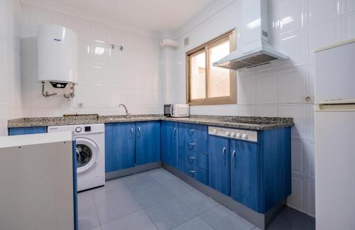 cocina con armarios azules, lavadora y secadora en Apartamentos Proamar, en Torre del Mar