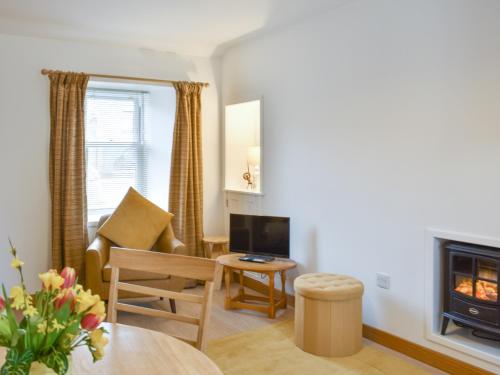 a living room with a fireplace and a chair at Rinnes Cottage in Aberlour
