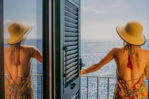 a woman in a hat looking out a window at the ocean at Il Baluardo Sea View Apartment on the Cliff in Manarola