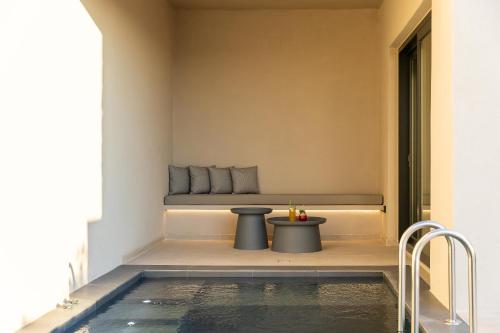 a room with a bench and a table next to a pool at North Santorini - A Luxury Spa Hotel in Pirgos