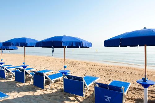 a row of blue chairs and umbrellas on a beach at Hotel Sierra Silvana in Selva di Fasano