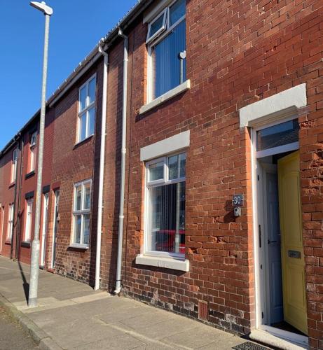 a brick building with a yellow door on a street at Cosy Seaside Hideaway in Northumberland with 1 pet welcome from November to March in Newbiggin-by-the-Sea