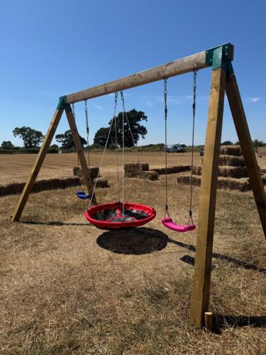 a swing set with three swings in a field at Shoreline Escapes at Hawthorn Field in Bransgore