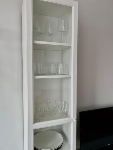 a white cabinet filled with glasses and bowls at Apartamentai Vanagupės banga in Palanga