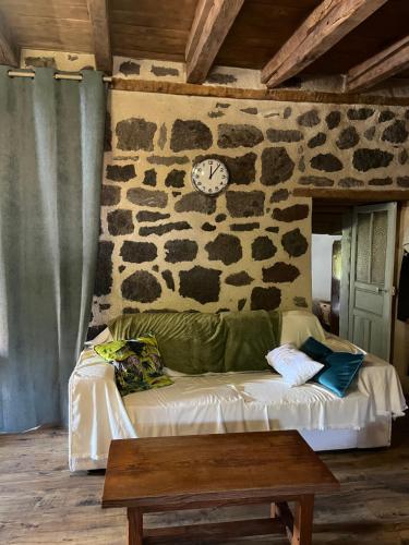 a room with a couch and a clock on a stone wall at La maison des petites choses, la tiny house du Puy Mary-Cantal in Lascelle