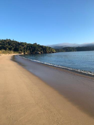 a sandy beach with water and trees in the background at Casa natureza in Paraty