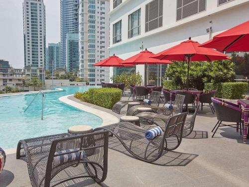 a patio with tables and chairs and a pool with red umbrellas at Acqua at The Hotel Residences Acqua Manila near Makati and BGC in Manila