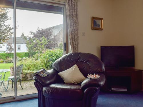 a leather chair in a living room with a large window at Craigrossie Cottage in Auchterarder