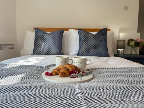a tray with two cups and two pastries on a bed at 2 bed Elegant Flat in Stansted with parking in Stansted Mountfitchet