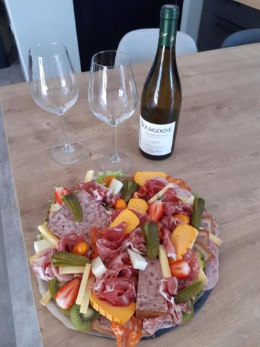 a plate of food with a bottle of wine and wine glasses at Gite de la perle rouge 1 Chambre 2-4 personnes in Rodelinghem