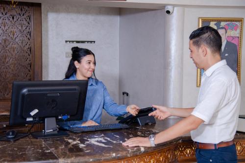 a man and a woman standing at a desk with a computer at Hotel Palais Al Bahja in Marrakech