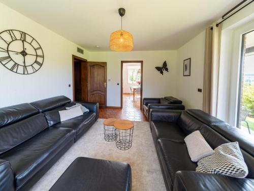 a living room with a black leather couch and a clock at Charming cottage in heart of the Ardennes in Lierneux