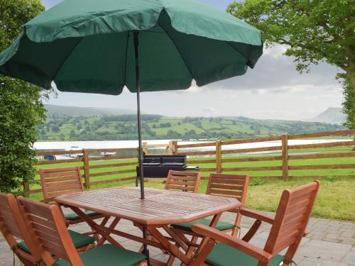 a wooden table with chairs and an umbrella at Bwthyn Glanllyn in Llanuwchllyn