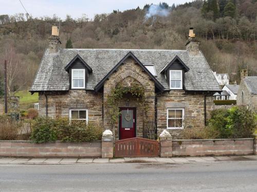 an old stone house with a red door at Smiddy Cottage in Aberfeldy