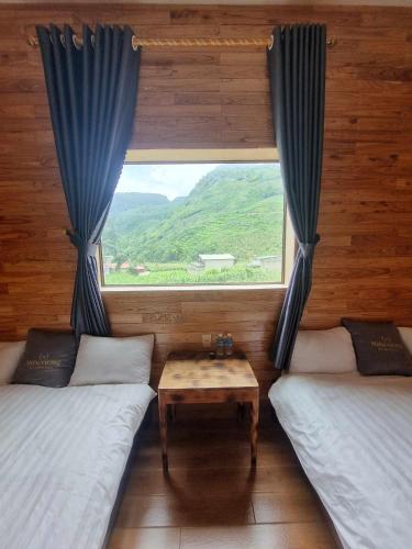 ein Zimmer mit zwei Betten und einem Fenster mit einem Tisch in der Unterkunft Miêu Vương Homestay Mèo Vạc in Mèo Vạc