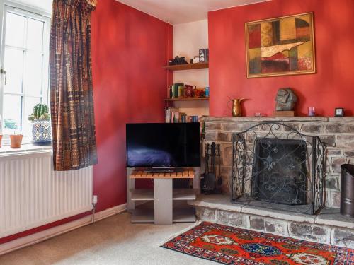 a living room with a fireplace and red walls at The Cottage in Blakeney